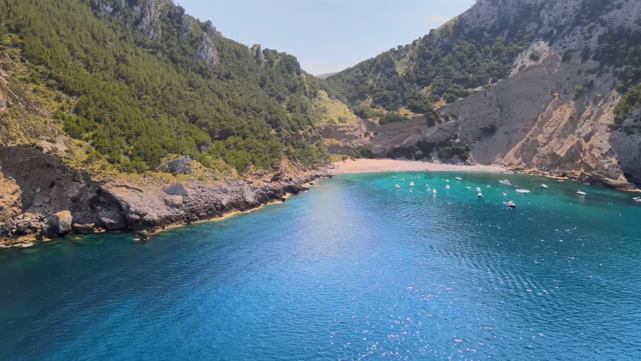 Explore the stunning coastline of Coll Baix, a secluded beach in Puerto de Alcudia, Mallorca. Experience the crystal-clear waters, rugged cliffs, and serene environment on a sunny day.