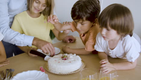 happy daddy helping excited daughter to cut festive cake