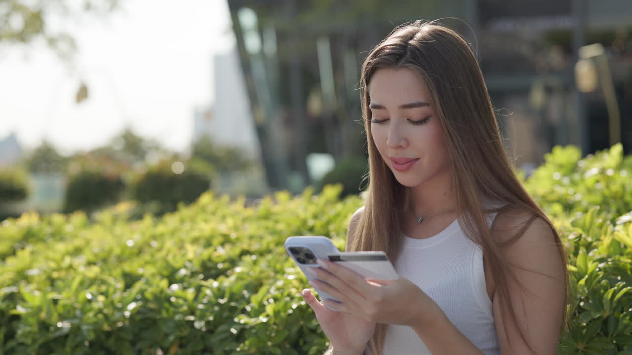 Woman using phone and credit card outdoors