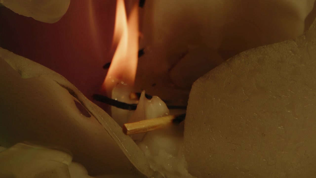 Smukt makrobillede af orange flammer, der brænder i slowmotion på en bunke voks fra et smeltet lys.