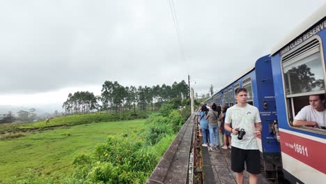 travelers take photos from a stationary train near great western station in talawakelle, sri lanka, surrounded by lush greenery and misty hills.