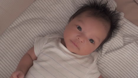 overhead portrait of a lovable baby in stripe lying in a bassinet