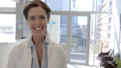 Portrait-of-happy-caucasian-female-doctor-smiling-in-hospital-reception,-copy-space,-slow-motion