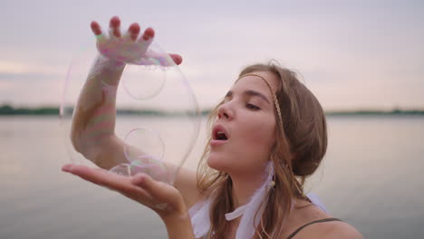 a young female artist shows a soap bubble show by blowing up large soap bubbles with her hands in slow motion