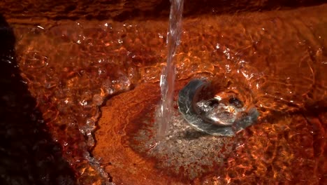 pan right to left of running water into a rusty sink of a public fountain