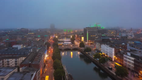 Los-Delanteros-Vuelan-Sobre-El-Río-Liffey.-Imágenes-Aéreas-De-Hiperlapso-Del-Tráfico-Nocturno-En-El-Paseo-Marítimo-Iluminado-Por-Las-Luces-De-La-Calle.-Nubes-Bajas-Sobre-La-Ciudad.-Dublín,-Irlanda