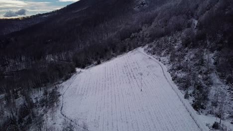 Spectacular-scenic-flight-above-snow-covered-farmland-in-rural-country-hillside-on-sunny-day,-overhead-aerial-tilt-down