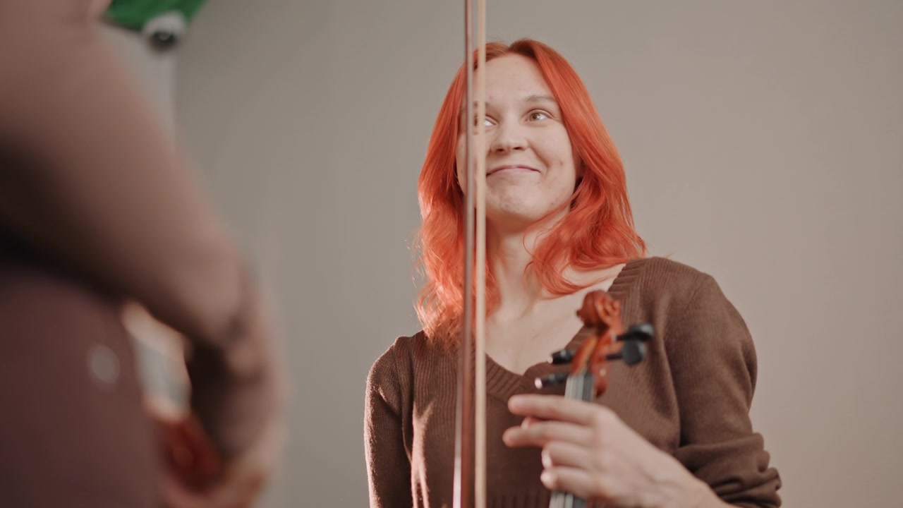 Violinista che riceve feedback dall'allenatore, musicista dai capelli rossi ascolta critiche e incoraggiamento, momento di conversazione in aula, sorriso sottile e postura attenta segnalano una reazione speranzosa