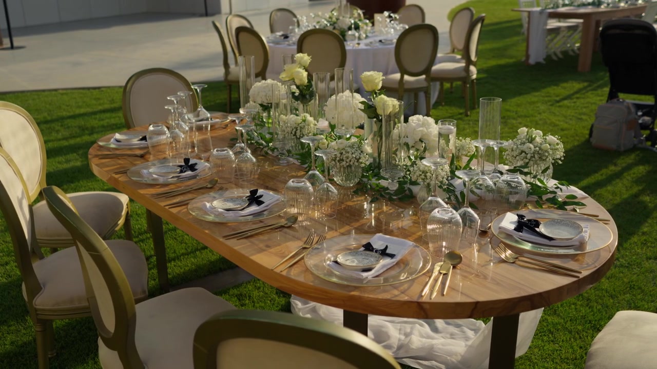 Oval wooden wedding table set with white flowers gold cutlery and glassware on a green lawn