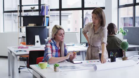 diverse female office colleagues discussing over blueprint plan at modern office