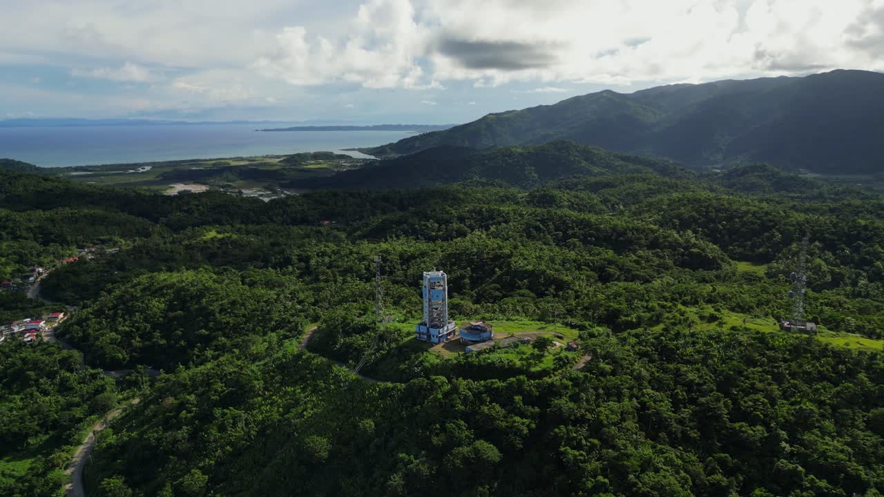 Aerial pullback of PAGASA weather radar station atop lush hills amid picturesque tropical island scenery and cloudscape