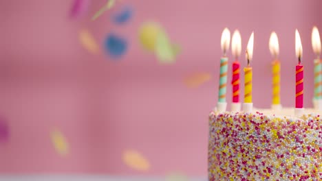 studio shot of paper confetti falling on birthday cake covered with decorations and candles being blown out