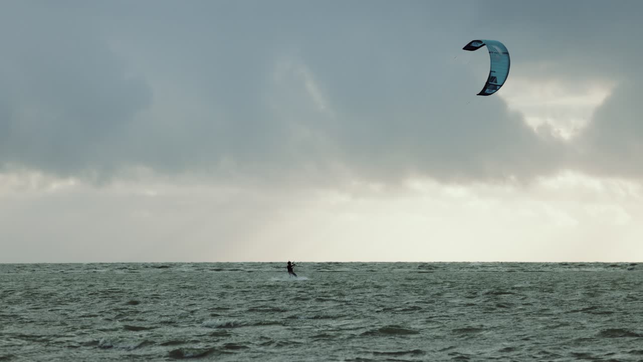 solo kitesurfista montando durante la tormenta en aguas azules perfectas, mientras el sol brilla a través de nubes oscuras