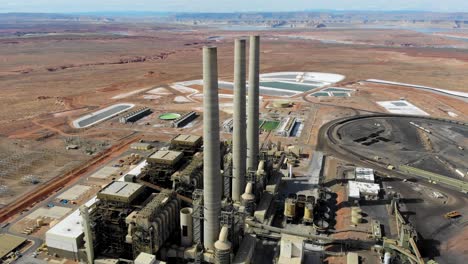 a drone shot of the “navajo generating station”, a massive coal-fired power plant and industrial complex with tall stacks, in the middle of the desert of the navajo nation, located near page, arizona