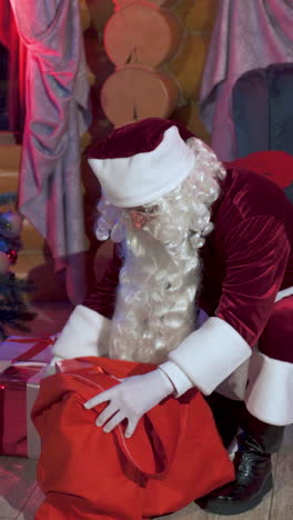 santa claus with a red sack indoors. real santa putting presents under the christmas tree quietly. vertical video