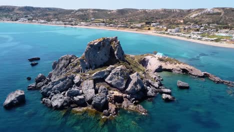 toma aérea cinematográfica de una formación rocosa en una paradisíaca isla griega con una pequeña iglesia en ella