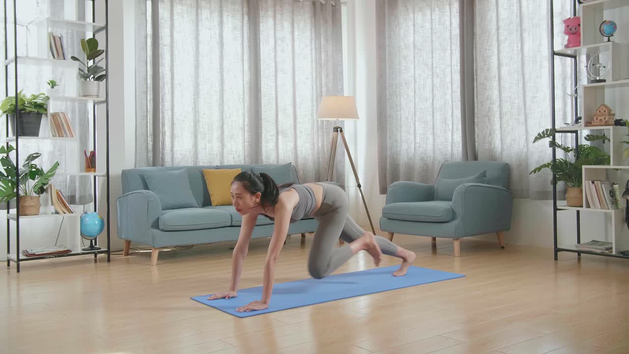 運動服を着た若いアジアの女性アスリートが自宅のマット上でのトレーニング中に膝を高くしコアを強化する運動をしています