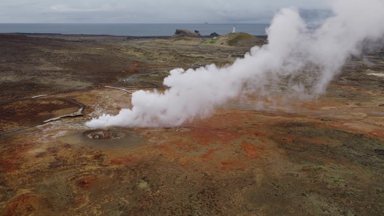 Gunnuhver geotermiska område, Reykjanesbær, södra halvön, Island, som avslöjar en kraftig ångplym, hydrotermiska avlagringar, förändrad vulkanisk mark och Reykjanesviti fyr, drönaröversikt.