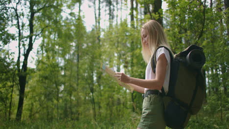 young woman traveler with map and backpack relaxing outdoor at nature trail on summer vacations day. lifestyle hiking concept. wood trip. picking direction with a map.