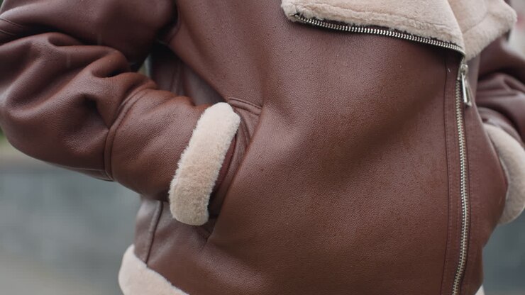Close up of person's brown shearling jacket with hands tucked in pockets, face not visible, showcasing rich texture and cozy design of winter outerwear worn on chilly day with blurred background