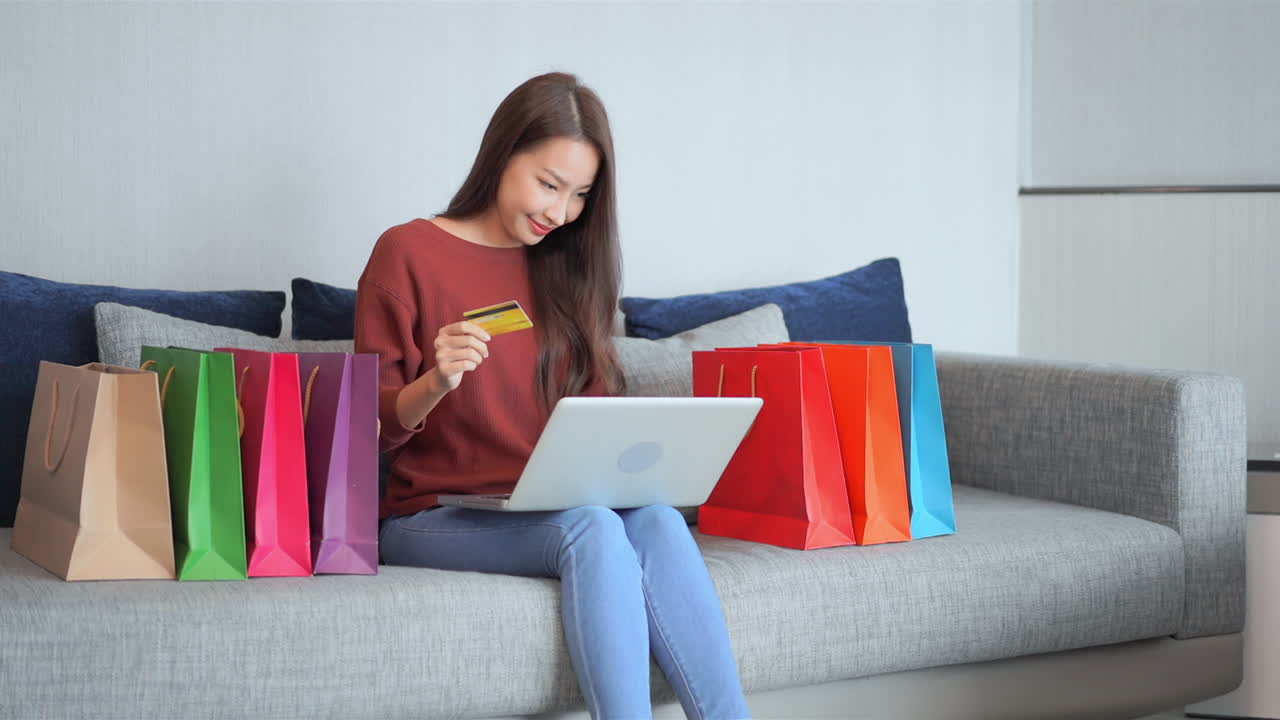 concepto de compras en línea, mujer bonita asiática comprando en línea con computadora portátil y tarjeta de crédito en un sofá lleno de bolsas, fotograma completo