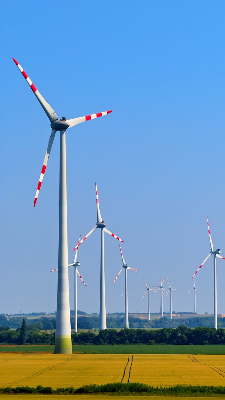 Wind turbines in a sunny landscape. Wind turbines rise against a blue sky, surrounded by golden fields and green hills, highlighting renewable energy