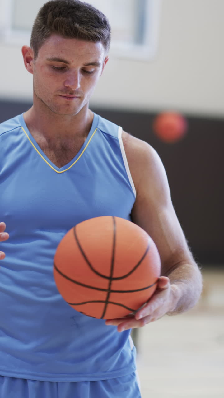Vertical video of male caucasian basketball player holding ball in indoor court, in slow motion