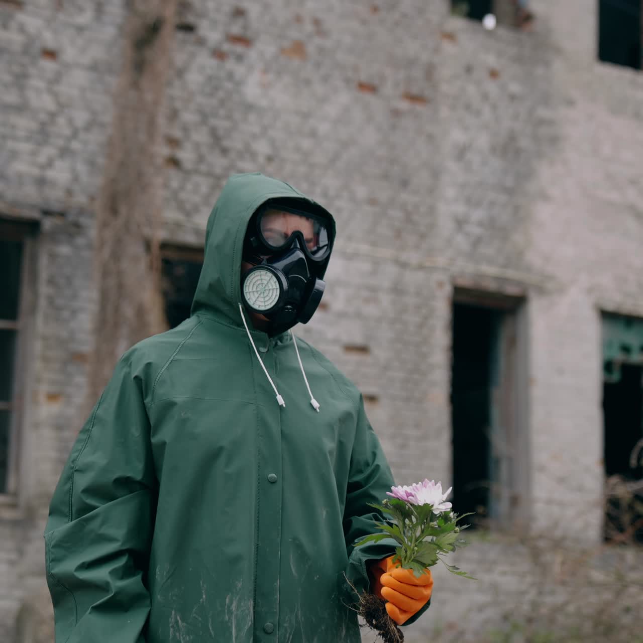 Save environment. Man wearing mask for breathing and protective suit holding flower against ruined building. Pollution of environment concept