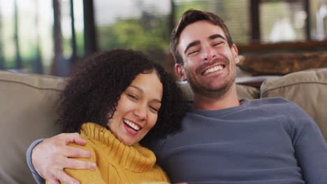Portrait-of-happy-diverse-couple-sitting-on-couch-in-living-room,-embracing-and-smiling