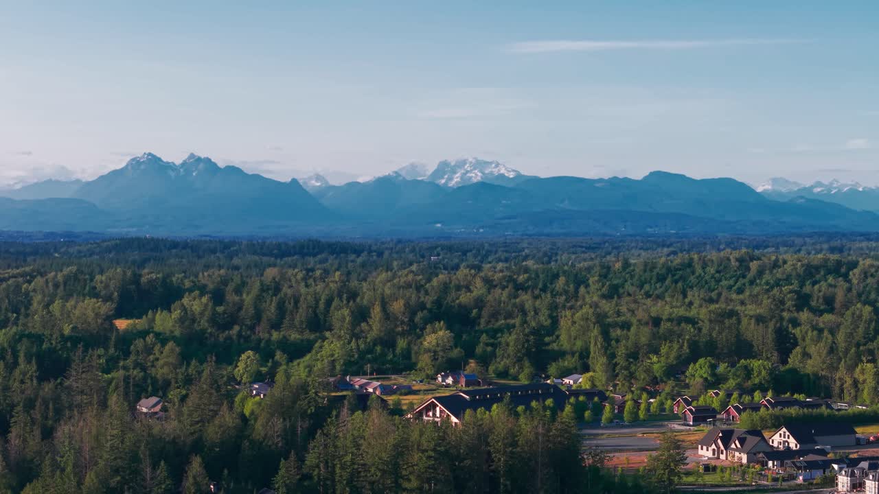A scenic view Mt Baker and several other mountains with luxury homes surrounded by lush green trees in Langley Township, British Columbia, Canada