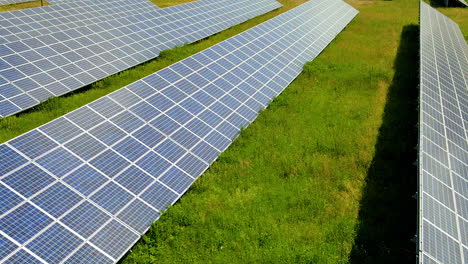 Aerial-backwards-flight-over-sustainable-and-eco-friendly-solar-panels-farm-surrounded-by-green-growing-grassland-in-sunlight