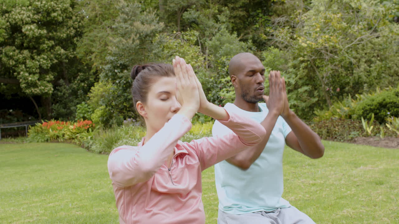 Meditating outdoors, diverse multiracial couple practicing yoga in garden setting, copy space