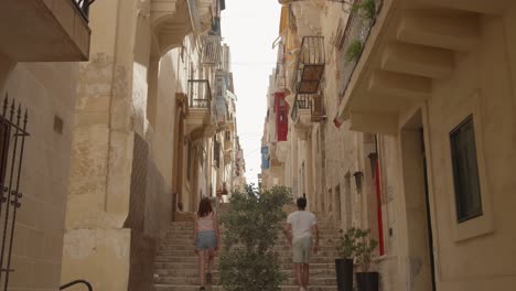 couple walking by a narrow old street in the city of senglea (isla), three cities, malta.