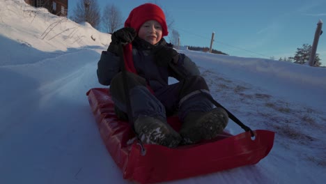 smiling young boy wearing red hat sledding down during christmas in innlandet, norway