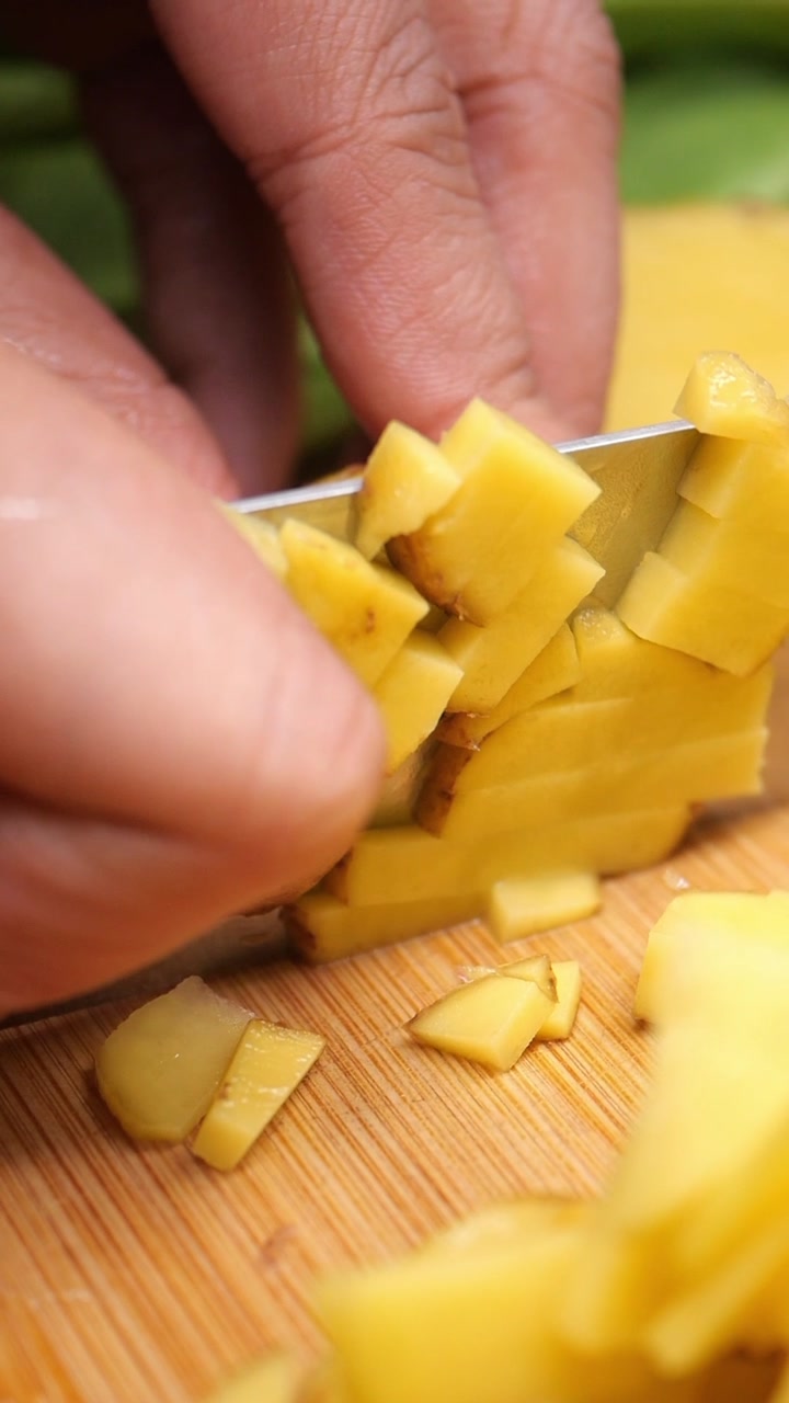 Close-up of Hands Chopping Fresh Ginger on a Wooden Board