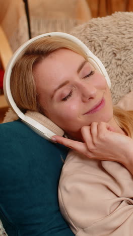 Woman lying on couch with eyes closed listening to music through headphones in peaceful relaxation