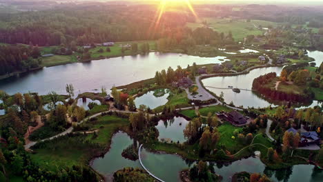 Toma-Aérea-De-Un-Hermoso-Parque-Con-Pequeños-Estanques-Y-Hermosos-Bungalows-Residenciales-En-Un-Barrio-Exclusivo-De-La-Ciudad-Al-Atardecer-Con-El-Sol-Poniéndose-Sobre-El-Horizonte