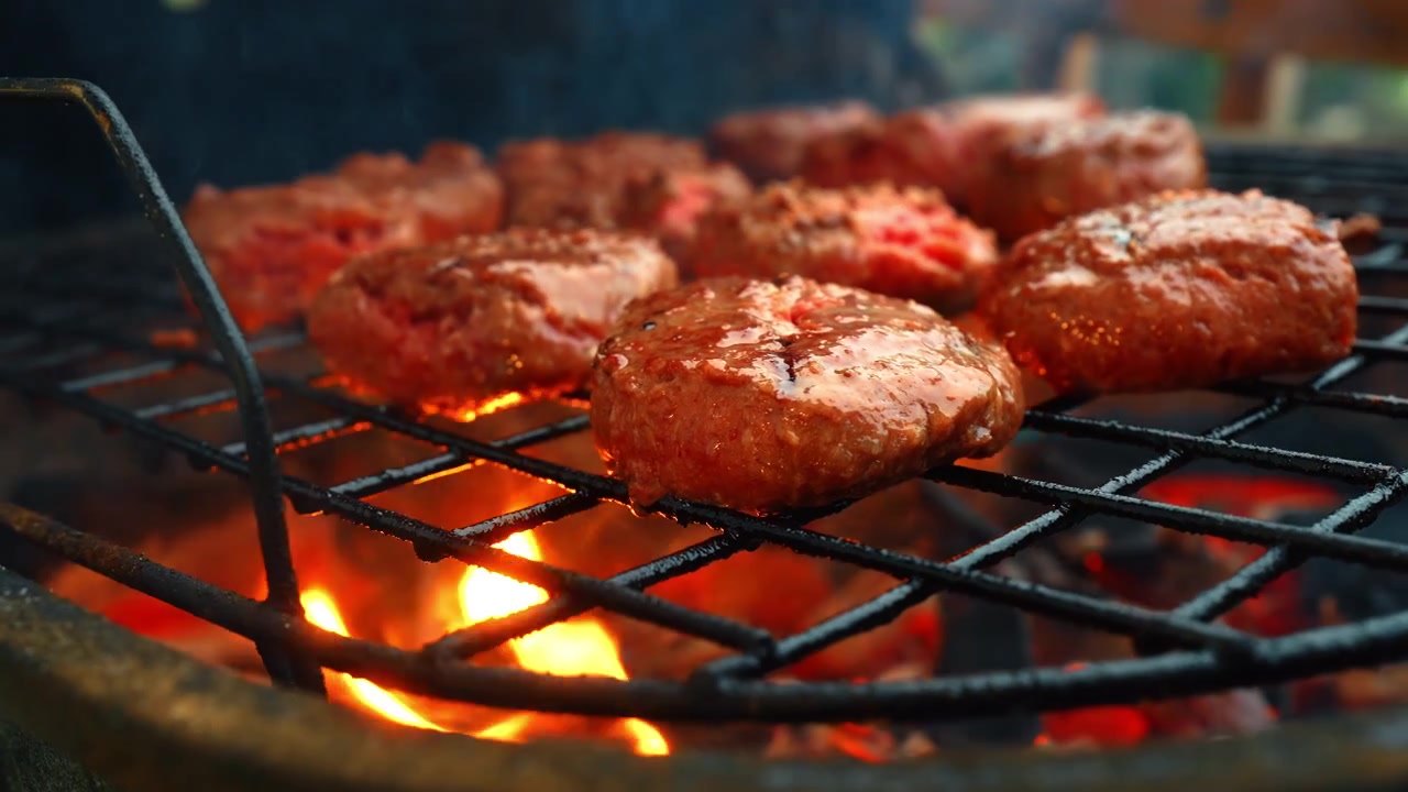 Hamburger di manzo che grigliano su fiamme vive su una griglia per barbecue. Diverse polpette di carne che cuociono su una griglia metallica con fuoco arancione brillante in un barbecue nero