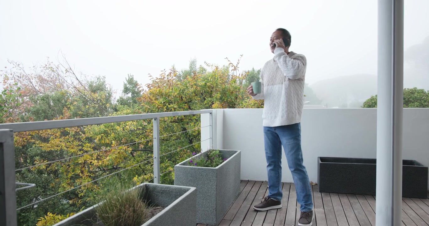 Homme chinois âgé répondant à un appel entrant, tenant une tasse, terminant l'appel et vérifiant son téléphone sur un balcon