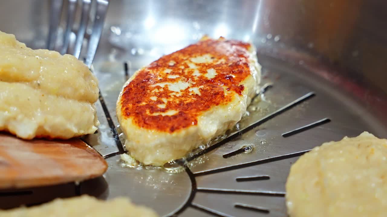 揚げ焼きされたカツレツがフライパンでひっくり返され、重なった質感と色彩で調理が続き、スローモーションで細部が見えます。