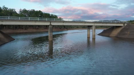 Drone-descending-and-flying-underneath-a-bridge-on-a-lake-near-to-Wivenhoe-Dam