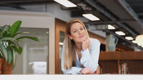 portrait of smiling casually dressed young businesswoman standing in modern open plan workplace