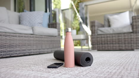 A-water-bottle,-yoga-mat,-and-smartphone-rest-on-textured-floor