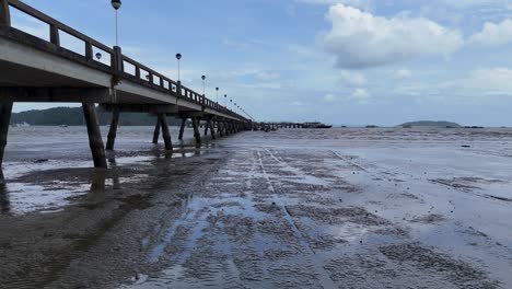 aerial footage captures a serene pier extending into the sea under a cloudy sky in phuket, thailand