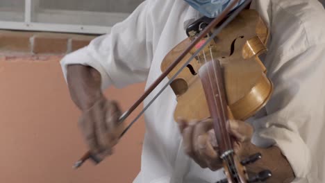 closeup shot of a hispanic aged musician with a hat and a mask playing violin on the street