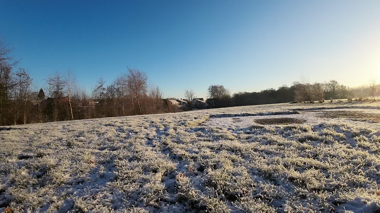 눈 덮인 겨울 초원 위의 나무 기둥을 통해 햇빛이 비치는 일출을 향해 날아가는 fpv