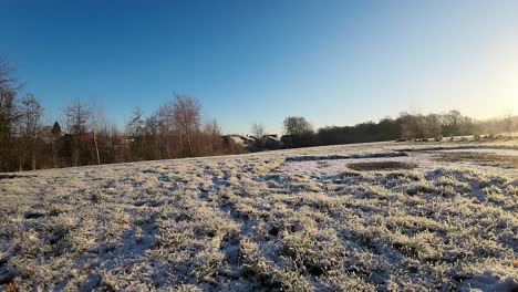 fpv flying through wooden posts over snowy winter meadow towards glowing sunlit sunrise