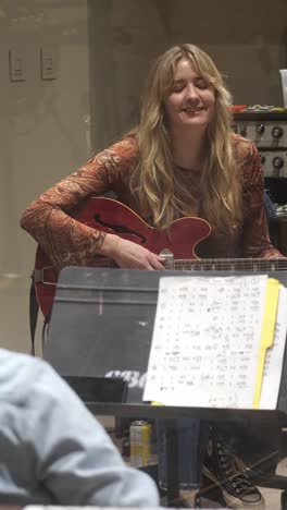 vertical - blonde-haired woman with electric guitar chatting and laughing during studio break. medium shot