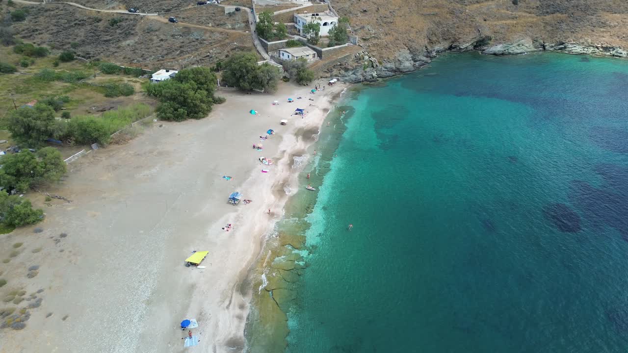 Sandy beach with towels and parasols alongside ocean with holiday homes in background