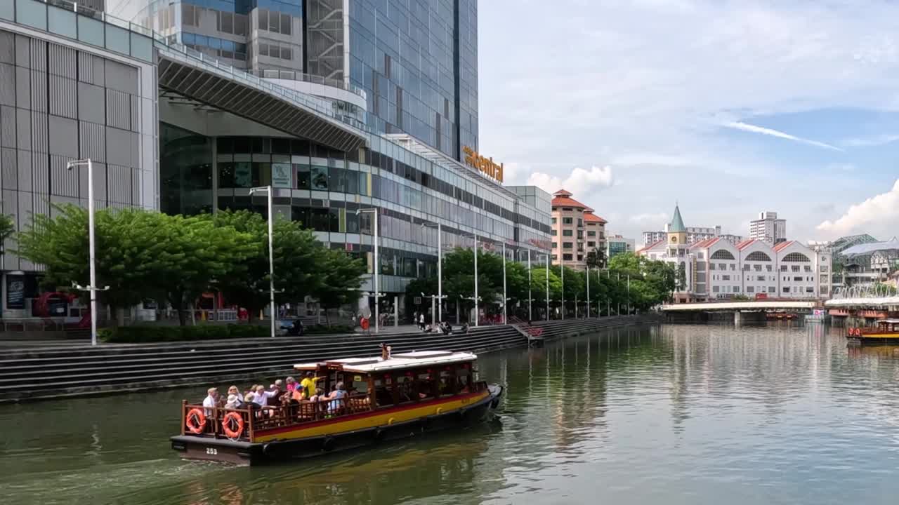 A boat navigates a city canal, flanked by modern buildings and lush greenery under a clear sky.
